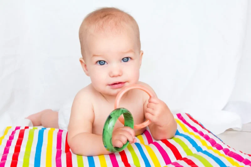 baby on a colorful striped blanket playing with ring toys
