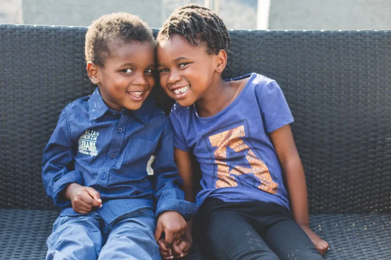 two smiling children sitting close together on a wicker sofa