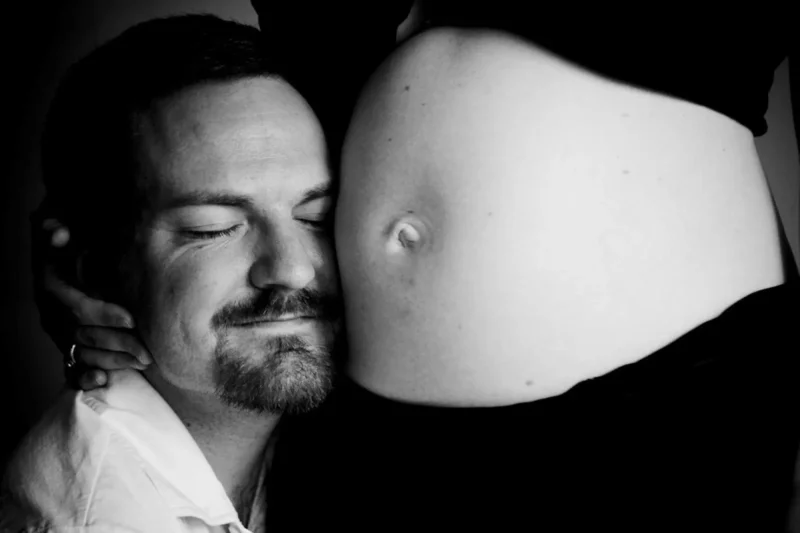 Black-and-white maternity portrait of a father kissing a pregnant belly