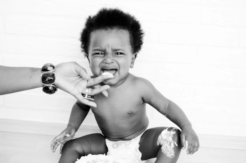 Black-and-white photo of a laughing baby being fed a cupcake