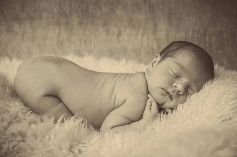 Newborn baby sleeping on its side on a soft cream fur blanket