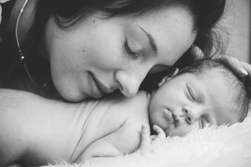Black-and-white photo of a mother resting her cheek against her sleeping newborn