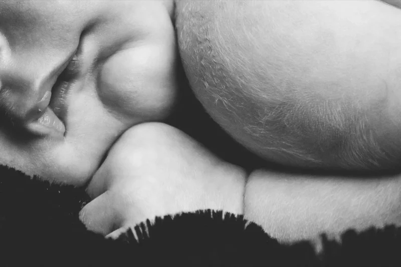 Black-and-white close-up of a pregnant woman resting her head on her belly