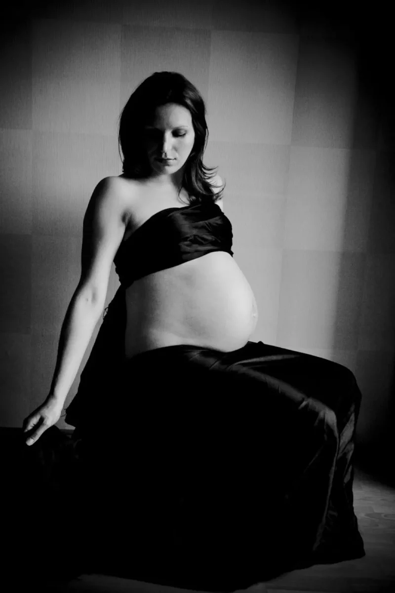 Black-and-white boudoir portrait of a pregnant woman wrapped in dark fabric