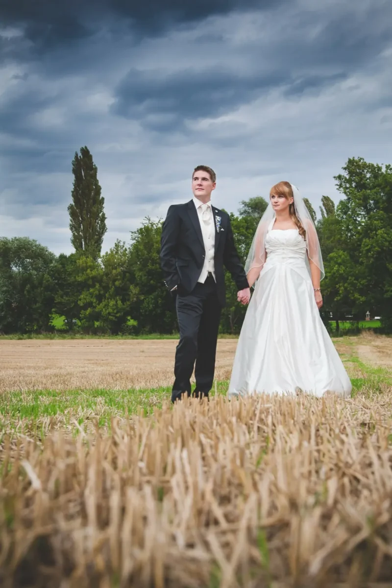 Bride and groom standing between storm clouds and a golden wheat field