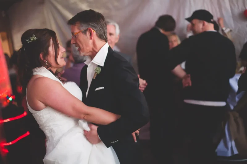 Newlyweds slow dancing at their reception, guests dancing behind them