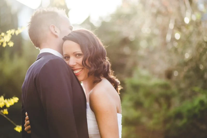 Smiling bride glancing back over her shoulder while embracing the groom in golden light