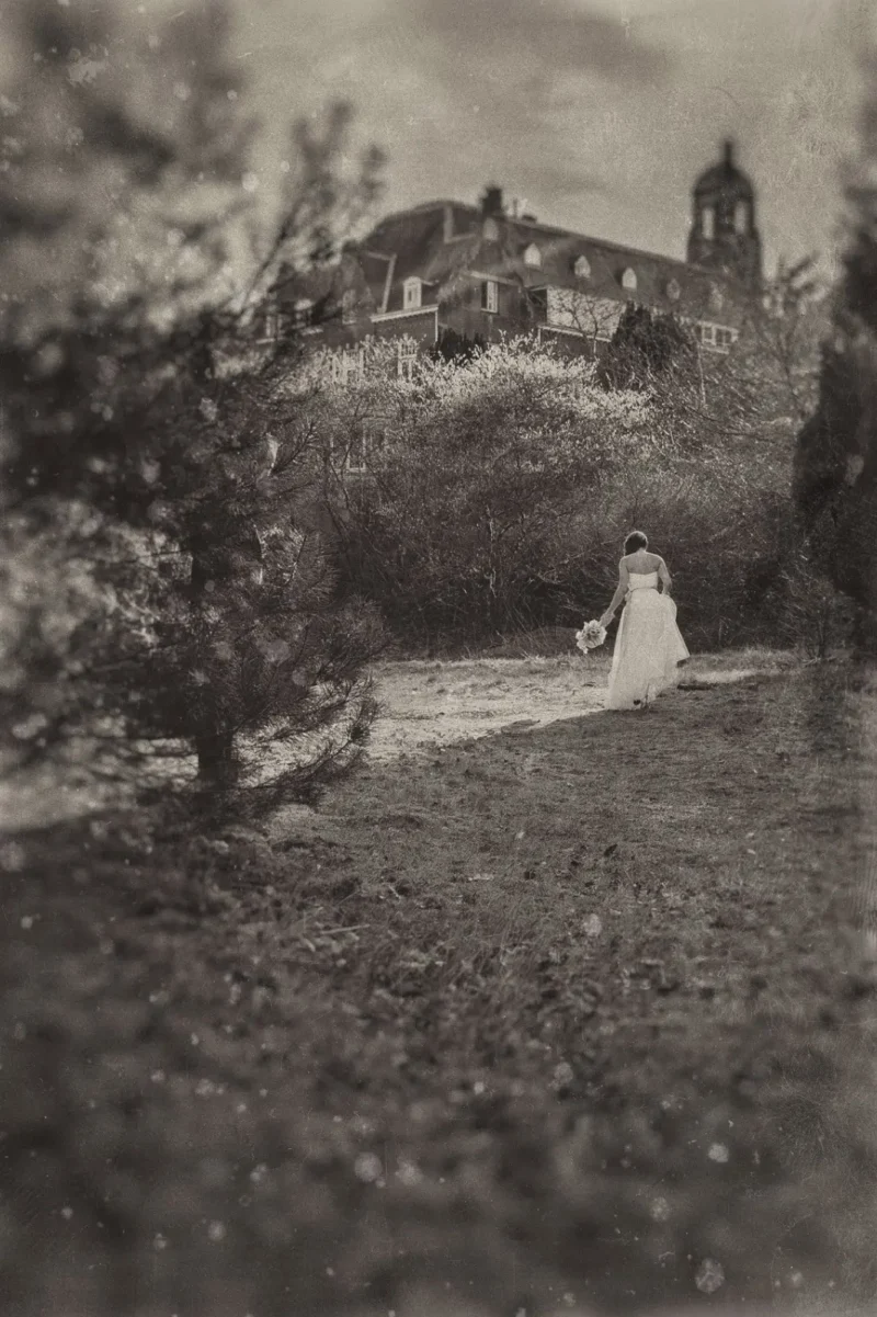Bride in white standing in a grassy orchard before an old hillside manor